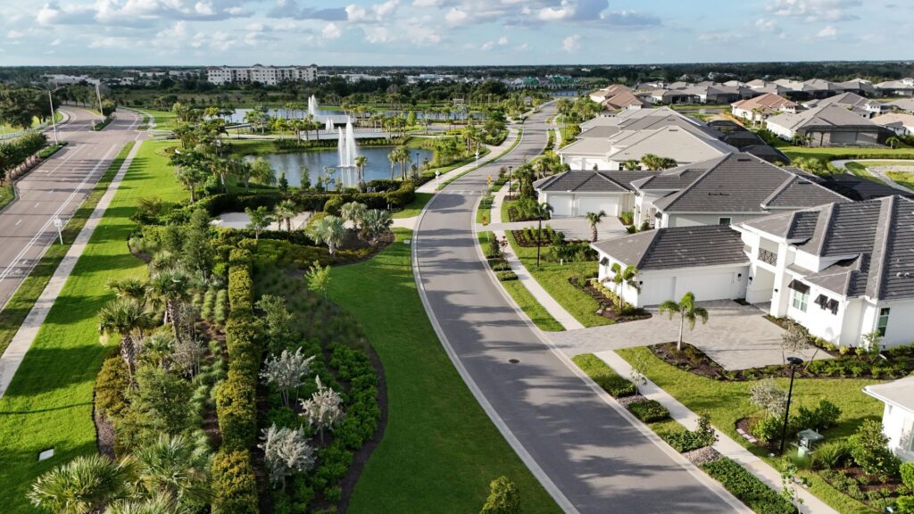 An aerial shot of a neighborhood featuring houses, a street, grass, trees, and a fountain.
