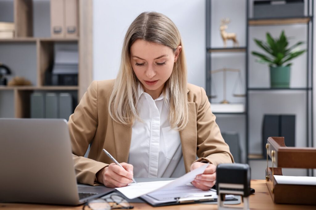 Blonde woman sitting at a desk with a laptop and paperwork