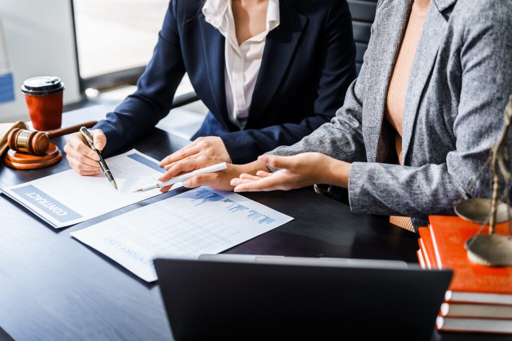 A female attorney sits next to a female client looking over a contract next to a laptop and a gavel resting on its stand.